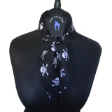 Lightweight cotton fabric scarf placed around a mannequins neck. Tied in a single loose knot around the neck with Nazine Alice Designs branded label. The fabric is an alternative gothic styled print of black background and white skull and crossbones