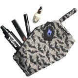 Coffin shaped makeup bag made with gothic fabric. The image shoes various makeup items inside, it can fit a lipstick, mascara, setting spray and highlighter. It has a coffin tag with the Nazine Alice Designs Logo on it.