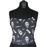 Front view of the ghostface crop top on a mannequin showing how the fabric stretches over the bust and waist. The fabric is a dark grey background with red blood splatters, the ghostface mask, a 90s wireless house phone, a voice changer and a knife.