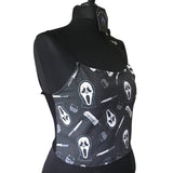 Side view of the ghostface crop top on a manniquin showing how the fabric stretches over the bust and waist. The fabric is a dark grey background with red blood splatters, the ghostface mask, a 90s wireless house phone, a voice changer and a knife.