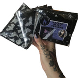 A hand holding up 3 different scarves folded neatly in recyclable clear packaging bags showing how they'll be received in the post with branded leaflet and stickers included.