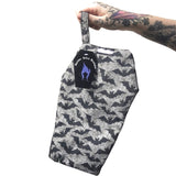 Coffin shaped makeup bag made with gothic fabric. It is a grey background with black lines of spiderwebs and black silhouettes of flying bats. It is being held by a tattooed hand.