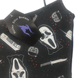 Close up of ghostface horror top, showing spaghetti strap elasticated shoulder detail. The fabric is ghostface from the scream films with a knife and blood splatters. The image also shows the Nazine Alice Designs coffin tag with the logo.