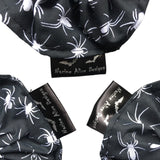 A gift set of three goth scrunchies in a Spiders fabric, it is a black background with white spiders all over as the pattern. This design is called 'Spiders'. The scrunchie has a luxury silk label with the brand name 'Nazine Alice Designs' on it.