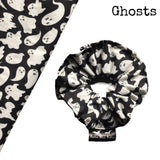 A goth scrunchie in a ghosts fabric, it is a plain black background with white ghosts all over as the pattern. This design is called 'Ghosts'. The scrunchie has a luxury silk label with the brand name 'Nazine Alice Designs' on it.