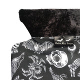 A goth hot water bottle made from an alternative fabric featuring skulls, crows, bats, tarantulas, eyeballs and sweets. It has a velvet top and a back opening. The lining fabric is a toweling fabric. I tcomes in giftable packaging. A black and white striped bag with stickers and a leaflet. On the front the bottle cover has a Nazine Alice Designs brand silk label sewn in.