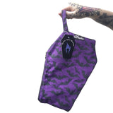 Coffin shaped makeup bag made with gothic fabric. It is a purple background with black lines of spiderwebs and black silhouettes of flying bats. It is being held by a tattooed hand.