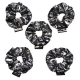 A set of five goth scrunchies in a gothic print fabric, a plain black background with white symbols of skulls, bats, spiders, skeletons, sweets and crows all over as the pattern. This design is called 'Trick or Treat'. The scrunchie has a luxury silk label with the brand name 'Nazine Alice Designs' on it.