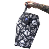 Coffin shaped makeup bag made with gothic fabric. It is a black background with white images of skulls, crows, eyeballs, spiders and bats. It is being held by a tattooed hand.