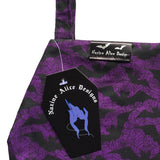 Close up of the coffin bats makeup bag, showing the details of the purple and black bats fabric, and showing the silk brand label sewn into the top giving it a luxury feel and look./ It has a Nazine Alice Designs coffin shape brand tag.